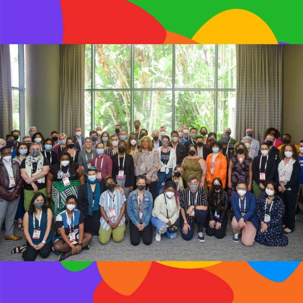 Dozens of participants of the ILGA World Conference are gathered in a conference room. Everyone is wearing masks and facing the camera