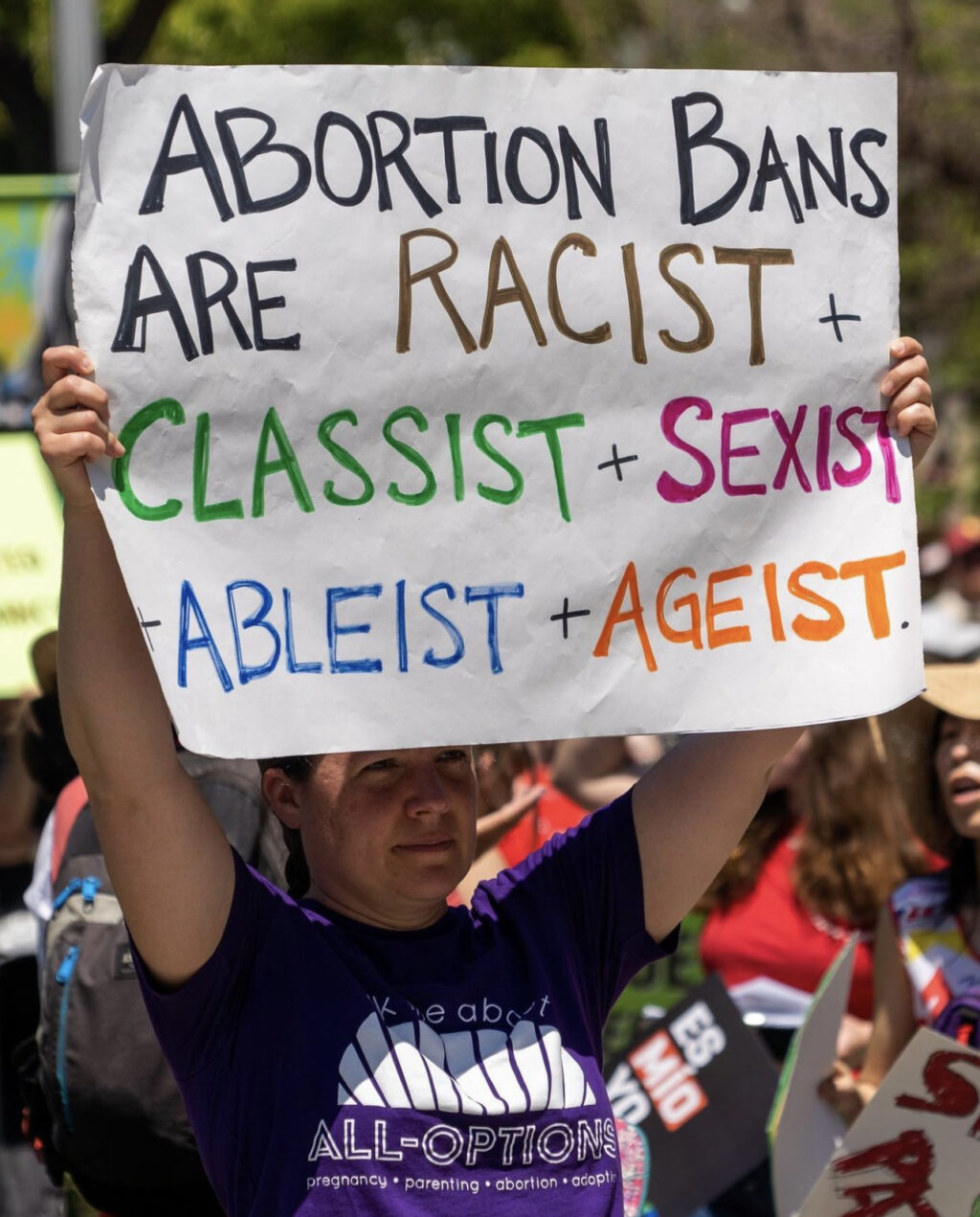 A pro-abortion protester holds up a multi-color sign that says “Abortion bans are racist, classist, sexist, ableist and ageist” at a protest, June 2022.